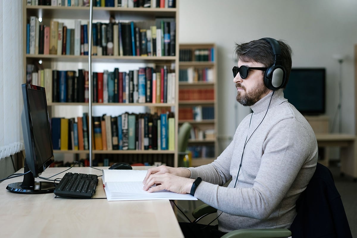 Blinder Nutzer bedient mit Kopfhörern einen Computerarbeitsplatz